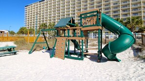 A beach playground with a slide and climbing structure, set against a backdrop of a large hotel building. - Summit 1 BR SLEEPS 5  ***BEACH CHAIRS INCLUDED*** (Panama City Beach)