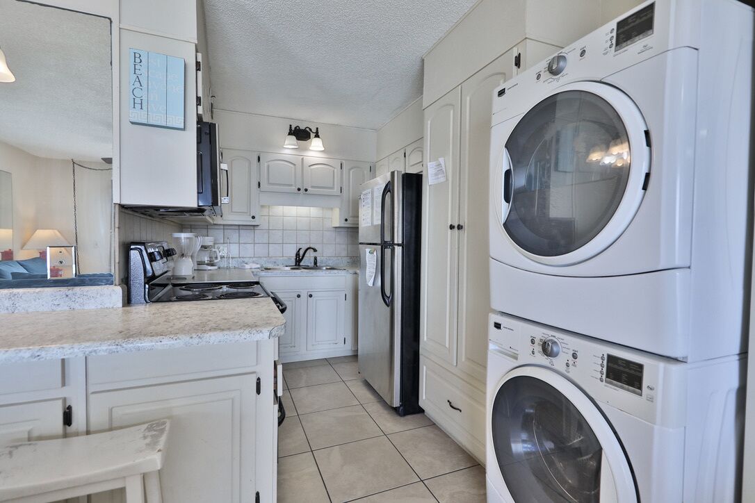 A compact kitchen with a stove, sink, and stacked appliances including a washing machine.