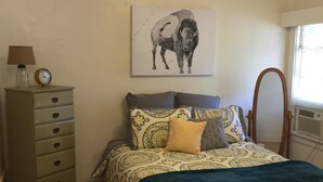 A bedroom with a bed, a dresser, a lamp, a clock, and a wall-mounted mirror.