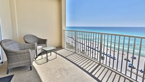 Ein Balkon mit Korbstühlen und einem kleinen Tisch, der auf einen Strand mit Sonnenschirmen und einen freien Blick auf den Ozean blickt.