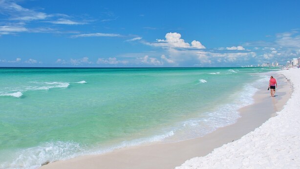 A beach with clear turquoise water, a sandy shore, and a distant city skyline.
