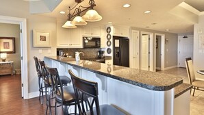 A modern kitchen with a central island, bar stools, a microwave, and a refrigerator.