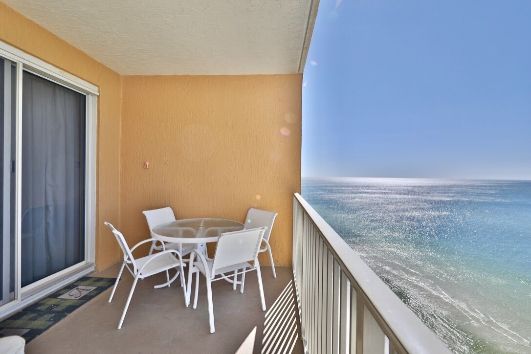 A balcony with a table and chairs, a sliding glass door, and a view of the ocean.