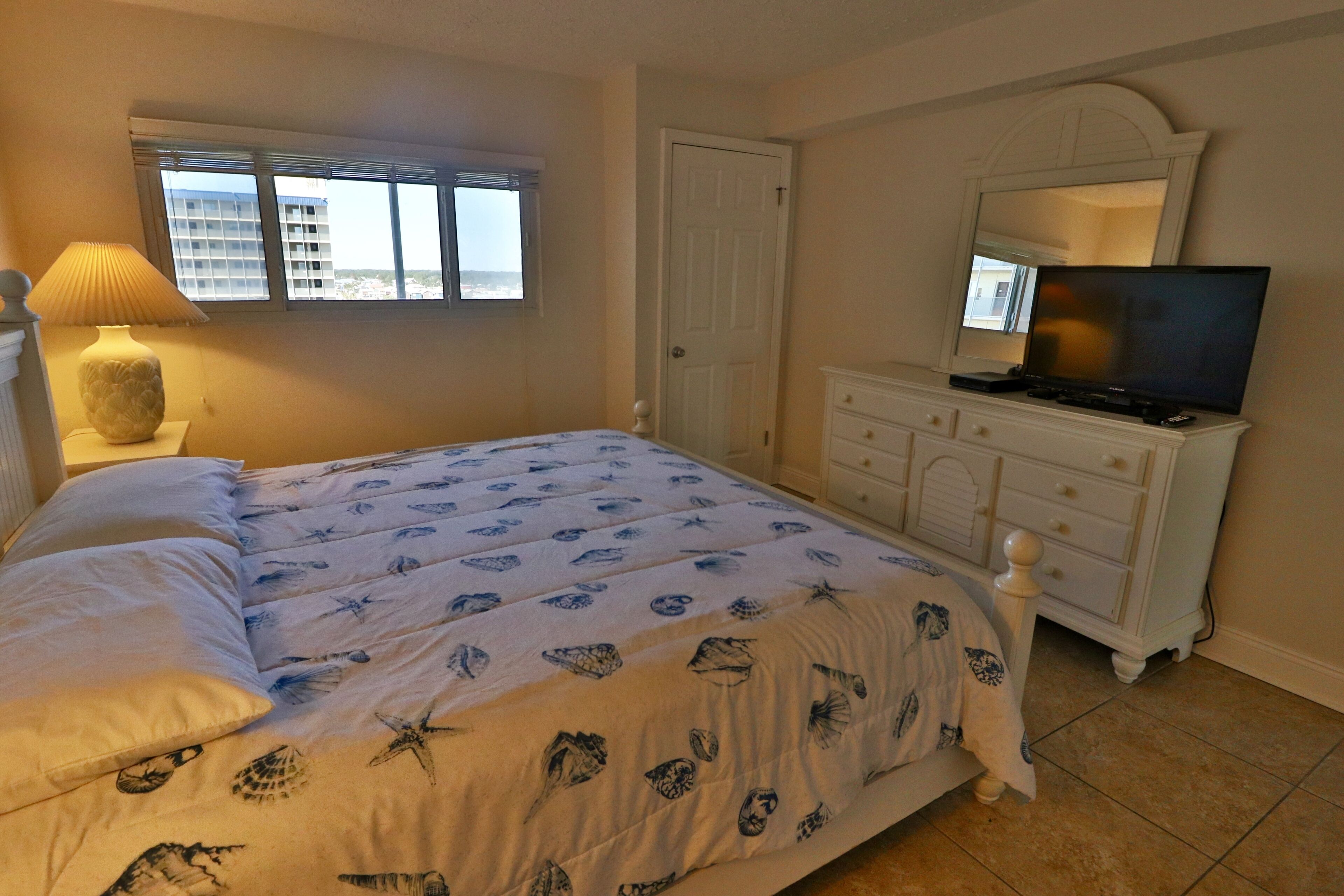 Un dormitorio con cama, cómoda, televisor y ventana con persianas.