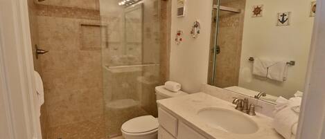 Un baño con ducha de vidrio, inodoro, lavabo y espejo.