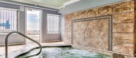 Un espace spa comprenant un jacuzzi, des murs carrelés et une vue sur l’extérieur.
