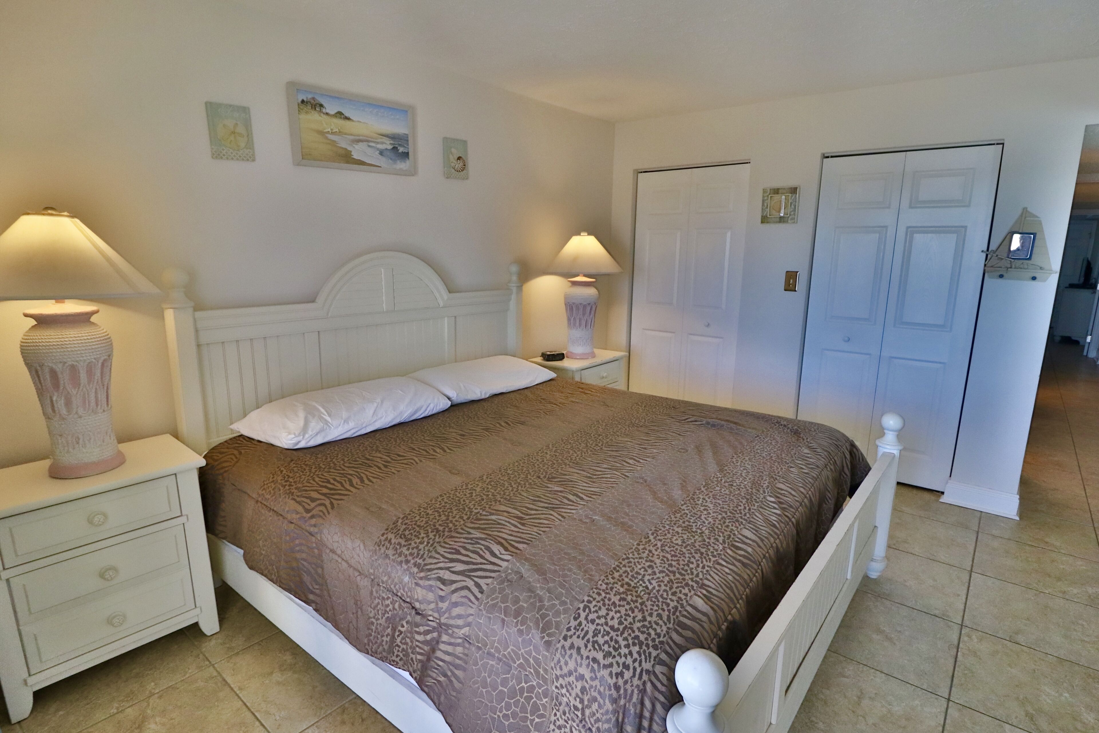 A bedroom with a bed, nightstands, lamps, a door, and a wall with two pictures.