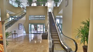 Un'ampia hall con un'escalatora centrale, diversi piani e piante in vaso.