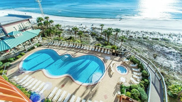 Un resort con una piscina grande, acceso a la playa y palmeras.