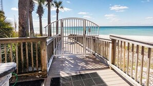 Una terraza de madera que da a una playa con palmeras y un cielo azul despejado.