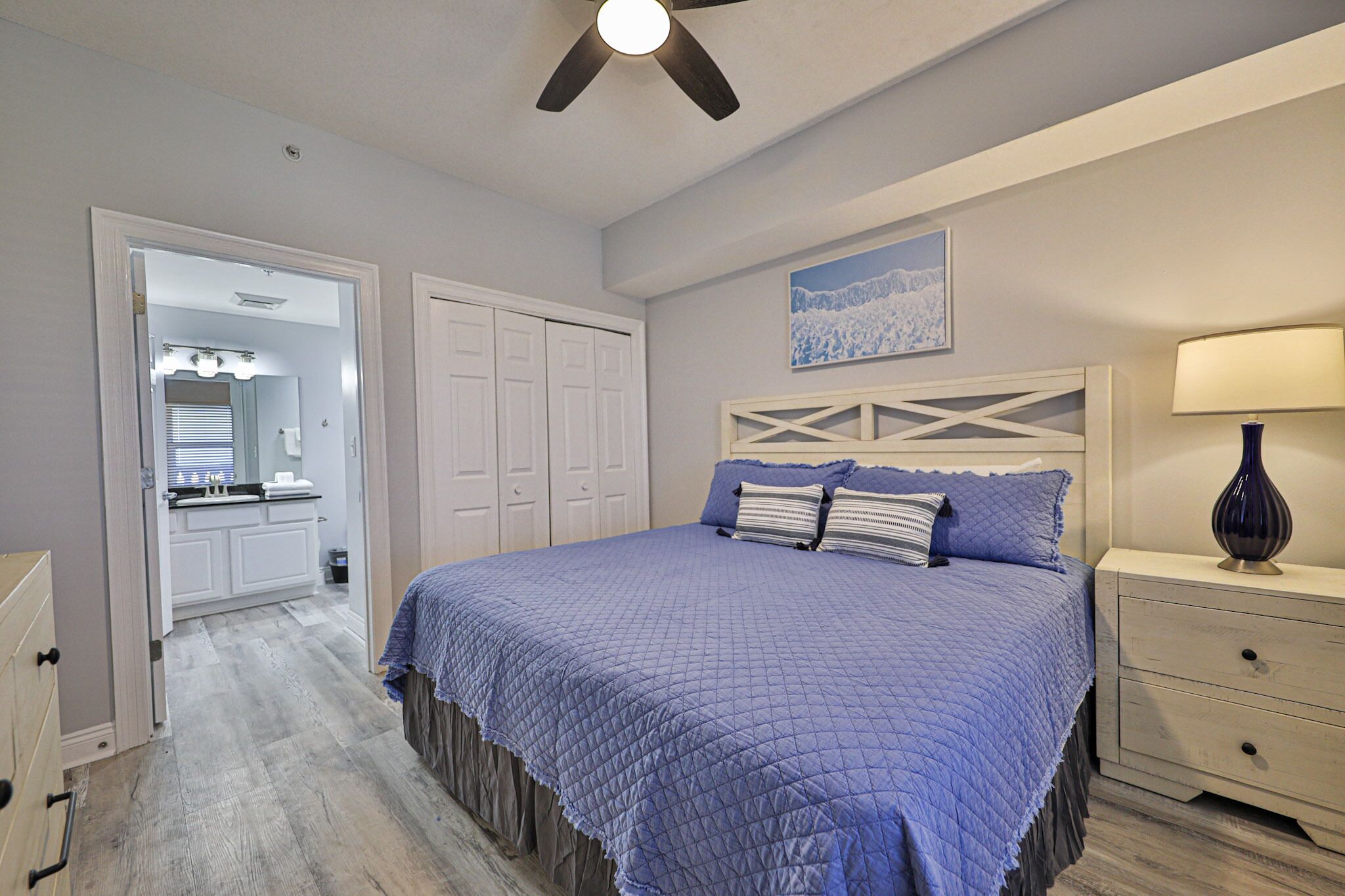 A bedroom with a large bed, a ceiling fan, a nightstand, and a dresser.