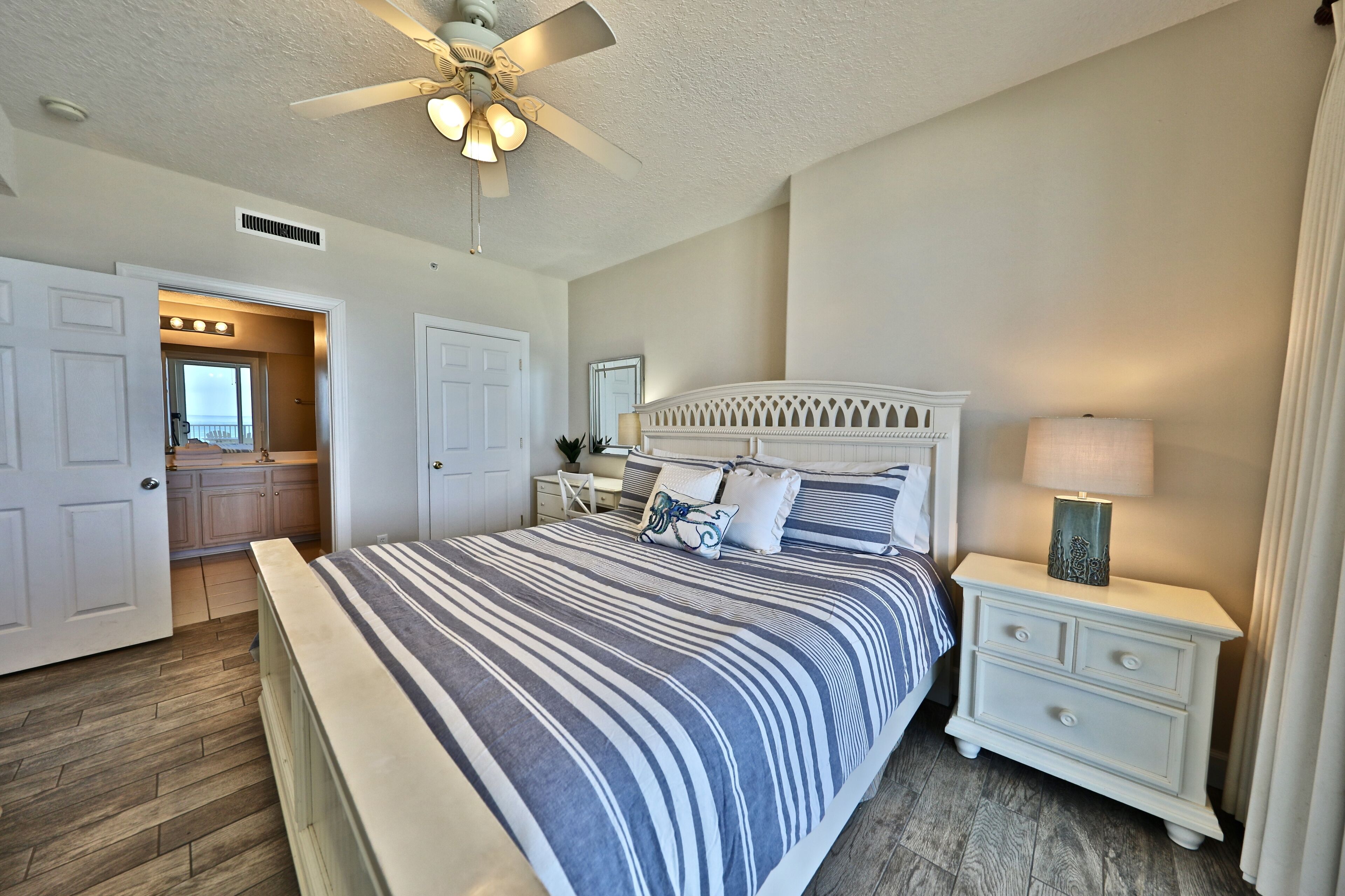 A bedroom with a large bed, a nightstand, a ceiling fan, and a bathroom visible through an open door.
