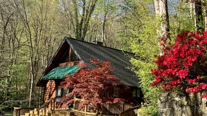 A cabin with a green roof, surrounded by a forest with red foliage and a stone wall.