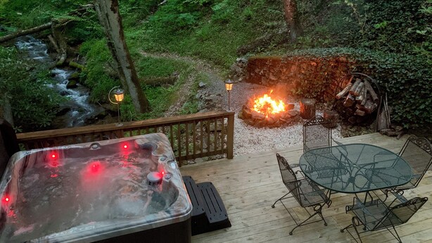 A hot tub on a wooden deck with a fire pit and outdoor seating.