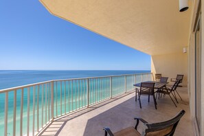 A balcony with a view of the ocean, a table, and chairs.