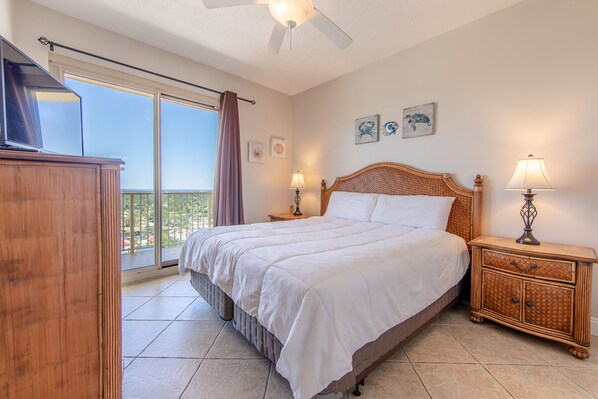 A bedroom with a large bed, a nightstand with lamps, a wooden dresser, and a balcony with a view.