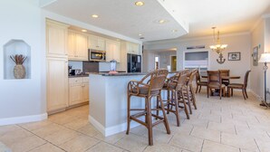 Una cocina amplia con armarios blancos, una isla central con taburetes y un comedor con candelabro.