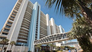 A modern high-rise building with multiple floors, a pedestrian bridge, and palm trees.