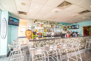 A bar area with a tiled backsplash, metal bar stools, and shelves stocked with various bottles.