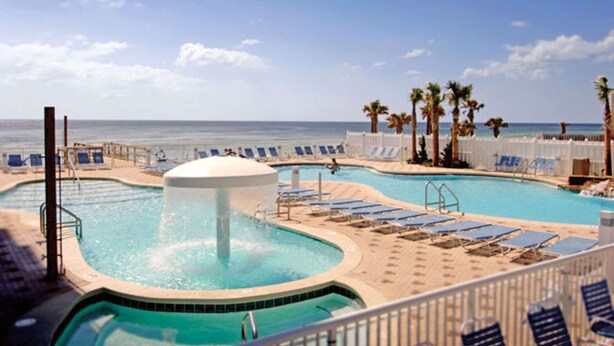 A pool area with multiple pools, lounge chairs, and palm trees.