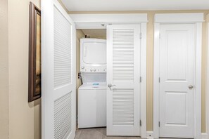 Un cuarto de lavado con lavadora y secadora, una puerta con picaporte y una rejilla en la pared.
