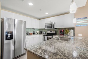 A modern kitchen with stainless steel appliances, a granite countertop, and a backsplash with hexagonal tiles. - Grand Panama 5th Floor Gulf Front, Same Level As Walkover! (Panama City Beach)