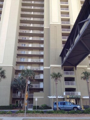 Un hotel de varios pisos con balcones, palmeras y un paseo techado.
