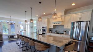 Una cocina moderna con una isla grande, electrodomésticos de acero inoxidable y lámparas colgantes.