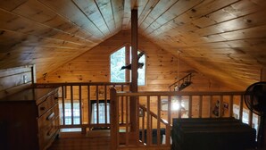 Un cuarto de madera en el ático con techo alto, una escalera y una ventana con vista a un bosque.