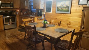 Enjoy meals in this cabin's dining area, featuring a wooden table and six comfortable chairs, a vase with a plant, and a beautiful landscape painting.
