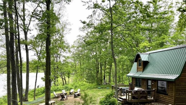 A cabin with a porch, surrounded by trees and a lake.