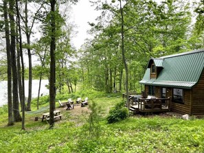 Une cabane dotée d’une véranda, entourée d’arbres et bordée par un lac.