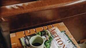 A leather sofa with a checkered pillow, a magazine, and a cup on a wooden coffee table.