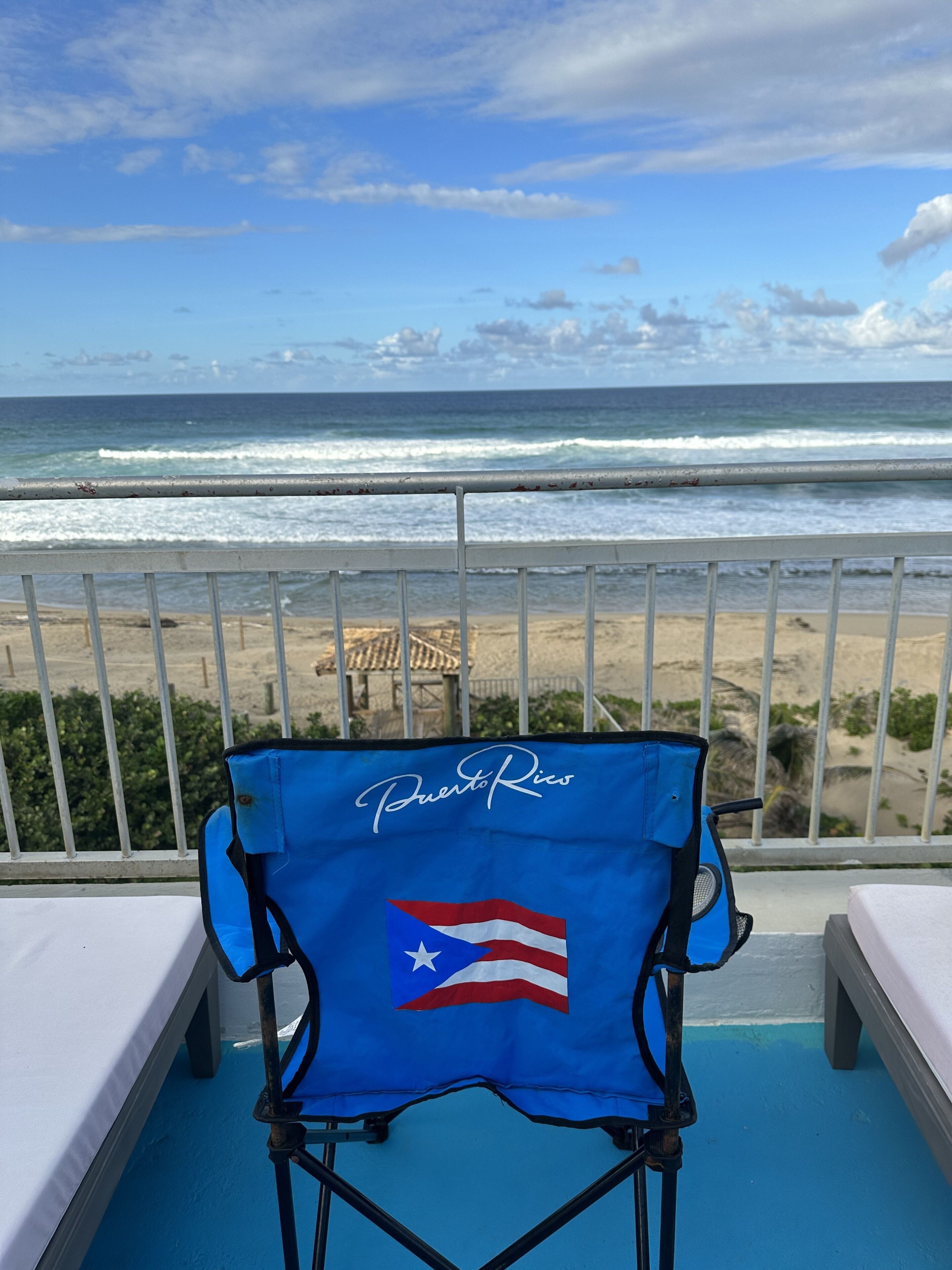 Una sedia blu con la scritta "Puerto Rico" e una bandiera, con vista su una spiaggia, le onde e un cielo sereno.