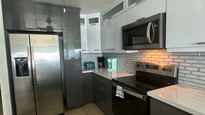 Een moderne keuken met roestvrijstalen apparatuur, witte kasten en een betegelde achterwand.