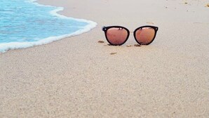 Een paar zonnebrillen op een zanderig strand met golven op de achtergrond.