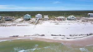 Une propriété située sur la côte, comprenant plusieurs maisons, une plage de sable et une zone boisée en arrière-plan.