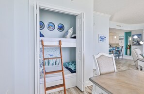 Una habitación con literas, una escalera de madera y una zona de comedor con mesa y sillas.