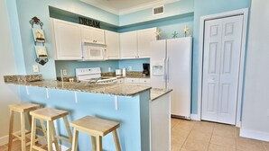 A kitchen with white cabinets, a granite countertop, and a built-in island with bar stools. - Tidewater 1011 10th Flr 2BR+Bunks 3BA Early Booking Discounts 2 Beach Chairs (Panama City Beach)