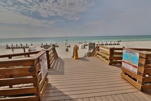 A wooden boardwalk leading to a beach with sun loungers and umbrellas.