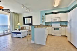 A compact kitchen with white cabinets, a microwave, and a refrigerator. There is a dining area with a table and chairs, and a balcony with a view.
