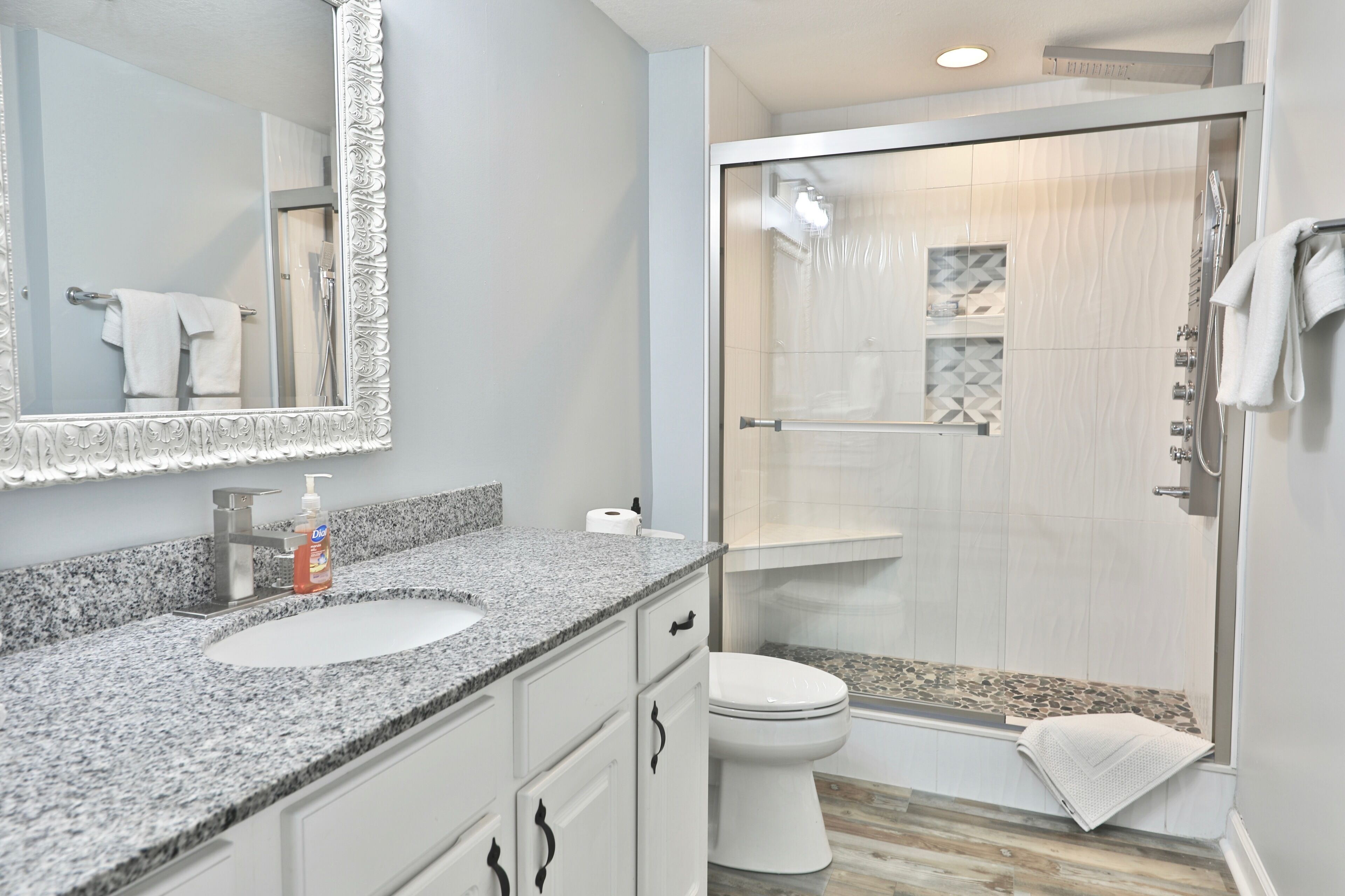 A bathroom with a granite countertop sink, a white toilet, and a glass-enclosed shower.