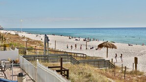 A beach with a wooden walkway leading to the water, a thatched umbrella, and people relaxing on the sand. - 1st floor 3br Marisol unit sleeps 8! (Panama City Beach)