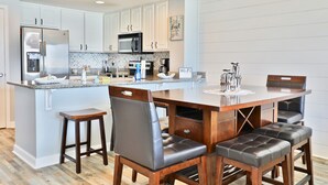 A modern kitchen with white cabinets, stainless steel appliances, and a wooden dining table with leather chairs. - 1st floor 3br Marisol unit sleeps 8! (Panama City Beach)