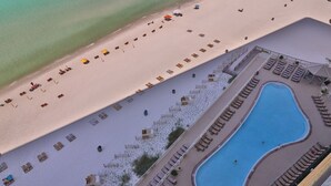 An aerial view of a resort with a beach, a pool, and sun loungers.