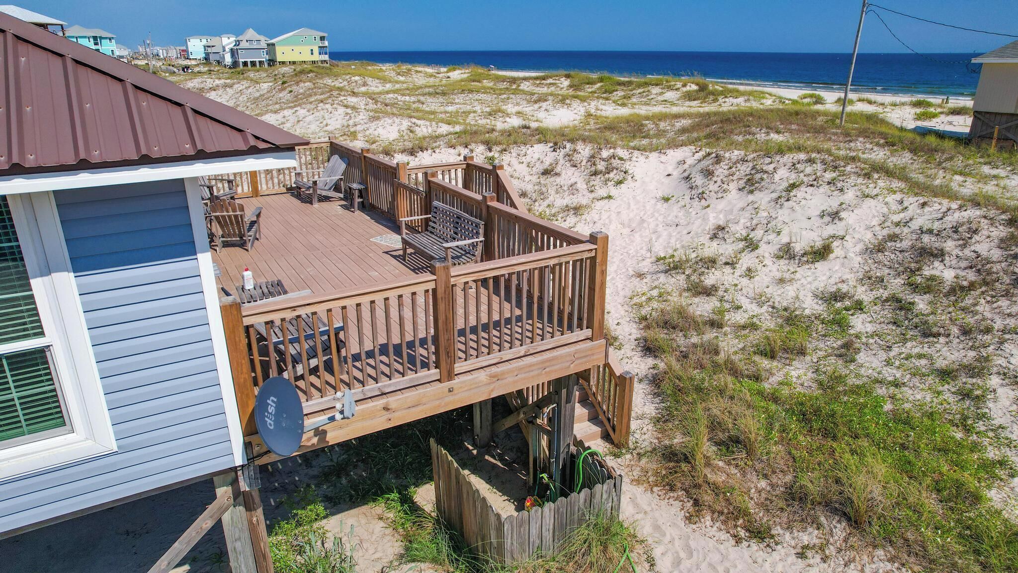 Ein Strandhaus mit Terrasse und Meerblick, ausgestattet mit Gartenmöbeln und einer Satellitenschüssel.