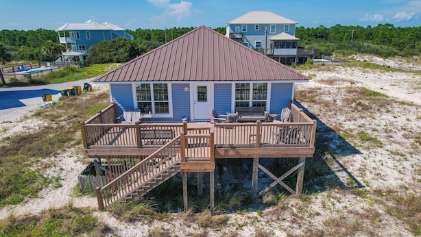 A beach house with a wooden deck, a staircase, and a view of the beach.