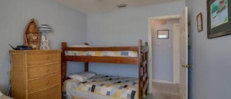 Un dormitorio con literas, un aparador de madera, un ventilador de techo y una puerta que da a otra habitación.