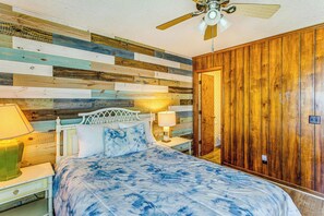 Ein Schlafzimmer mit einem Holz-Kopfteil, einem Bett mit blumigem, blauem Bettbezug, zwei Nachttischlampen, einem Deckenventilator und einem Holzschrank.