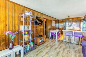 Una stanza con rivestimento in legno, un tavolo bianco, sedie viola, angolo cottura e una libreria viola.